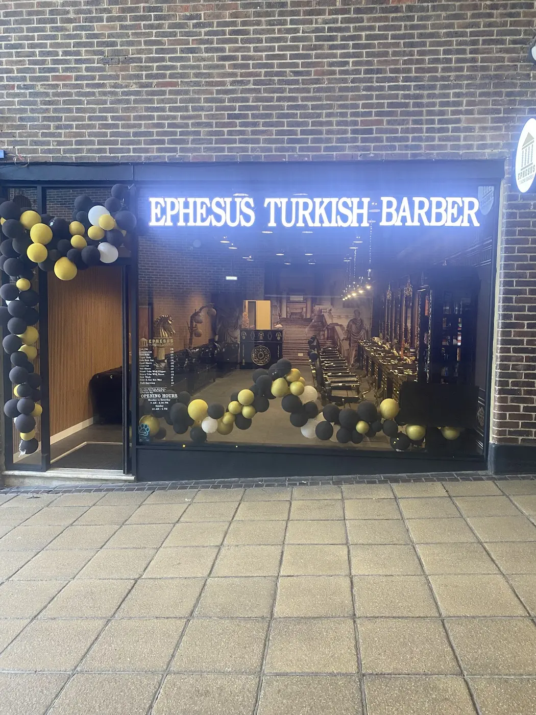 Lit white EPHESUS TURKISH BARBER sign above the shop window in Basingstoke, dressed with black and gold balloons
